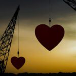 silhouette of construction cranes holding a heart