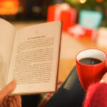 woman holding coffee reading book in front of Christmas Tree